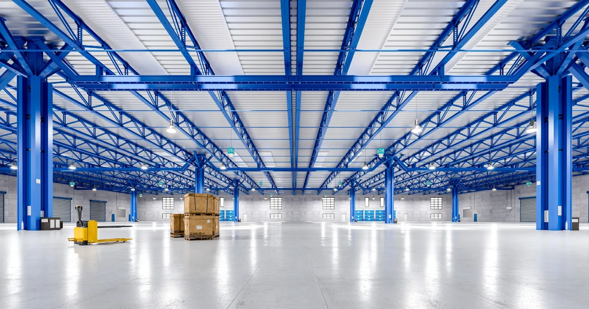 Grand entrepôt moderne avec colonnes en acier bleues, palettes et transpalette, illustrant un espace propre pour un déménagement fluide.