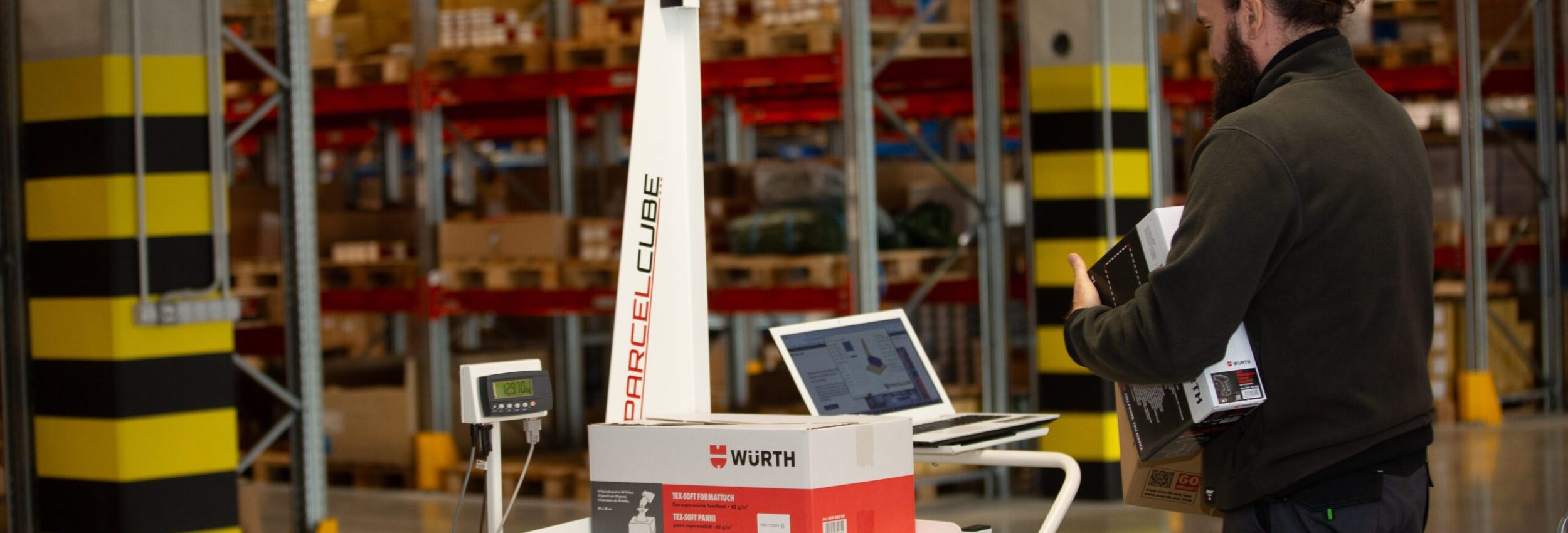 Parcelcube 900 in use at a Würth warehouse, measuring packages with shelves of inventory visible in the background.